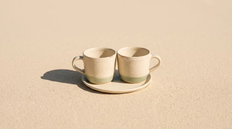 Two ceramic cups on a single shared saucer, their rims just touching