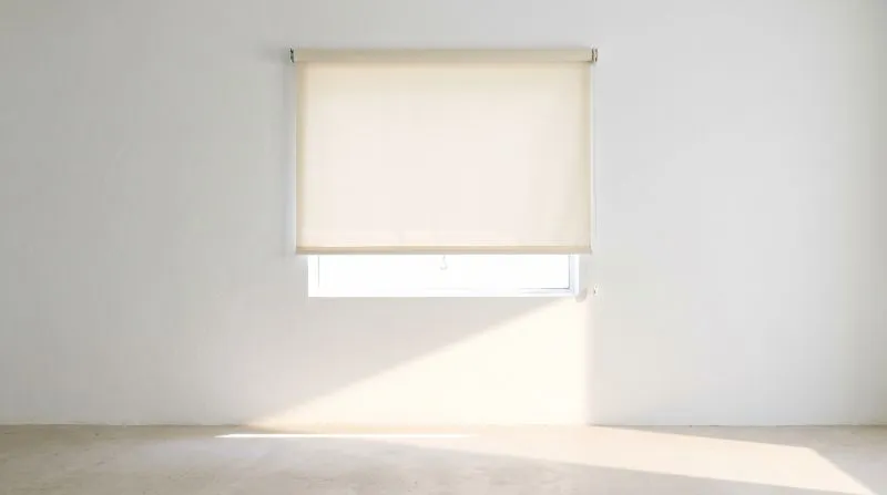 A blind raised halfway with bright daylight flooding across a pale wall