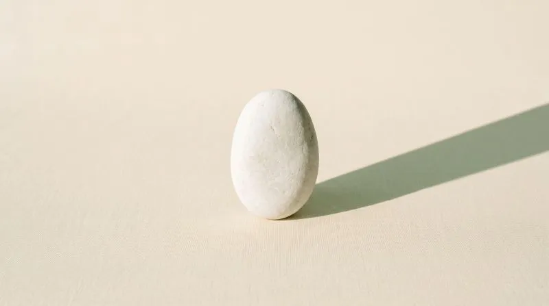 A single smooth stone standing balanced upright, casting one long shadow