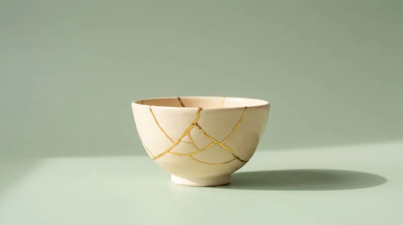 A cream ceramic bowl mended with visible gold kintsugi seams